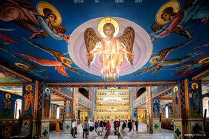 Ornate Byzantine-style church interior featuring a painted dome ceiling with religious iconography and golden chandeliers.