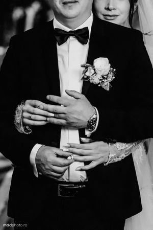Black and white wedding photo showing couple's hands embracing with groom wearing boutonniere and bow tie.