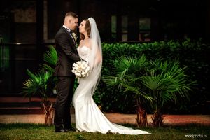 Elegant wedding couple embraces in front of tropical palm plants during an evening outdoor photoshoot.