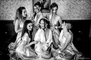 Black and white photo of a wedding party in matching silk robes sharing a quiet moment together on a bed.