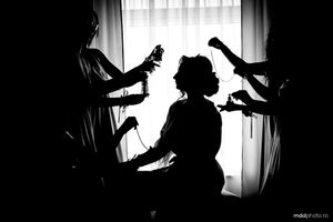 Dramatic silhouette of hairstylists working on a client's hair against a backlit window.