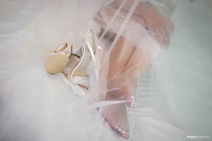 Elegant white wedding shoes with straps rest delicately on soft pink tulle fabric.