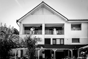 A black and white photograph of a two-story white house with a covered porch and multiple balconies.