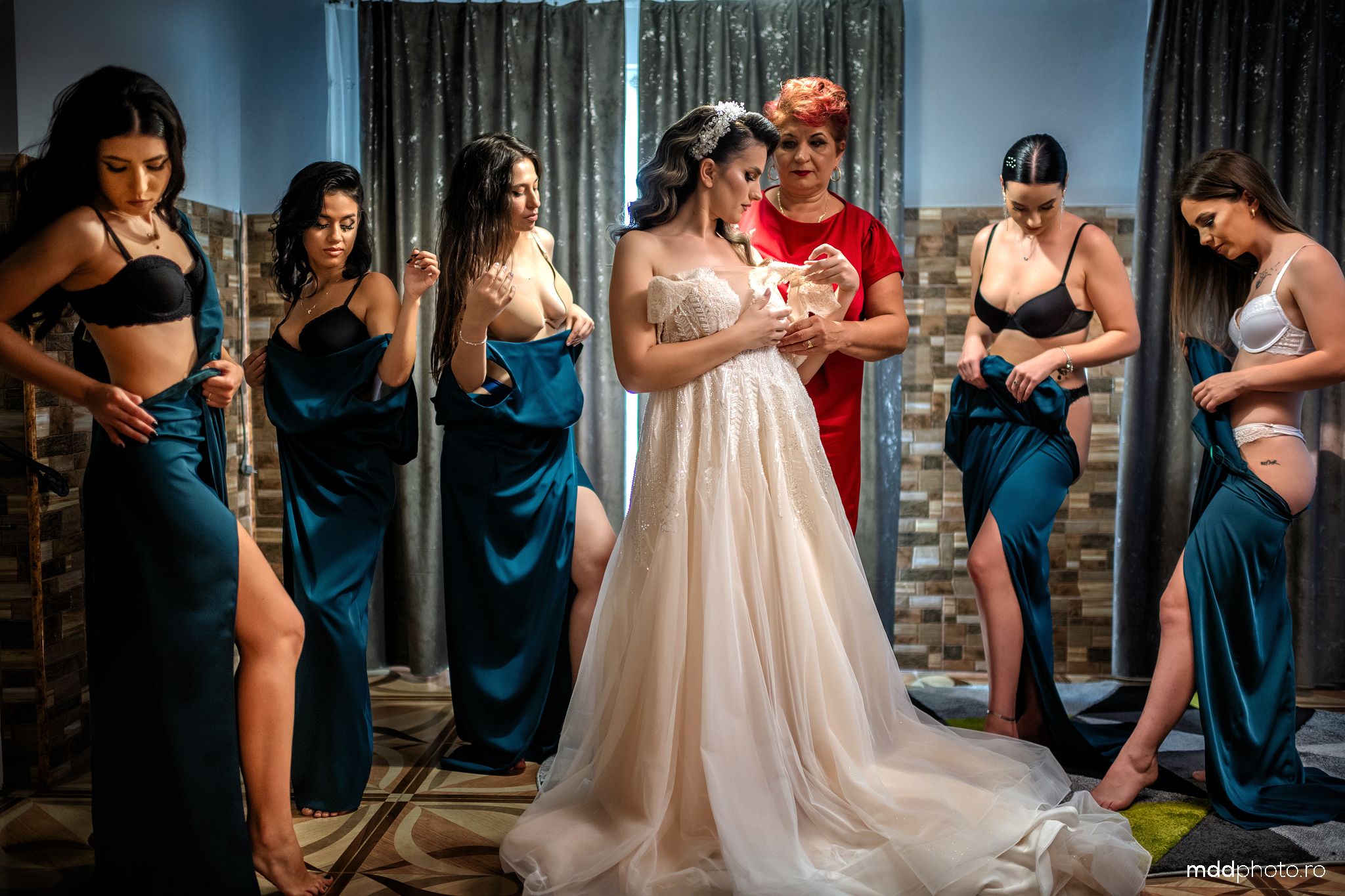 A wedding party poses together in a room with bridesmaids wearing teal satin dresses and displaying dramatic leg slits.