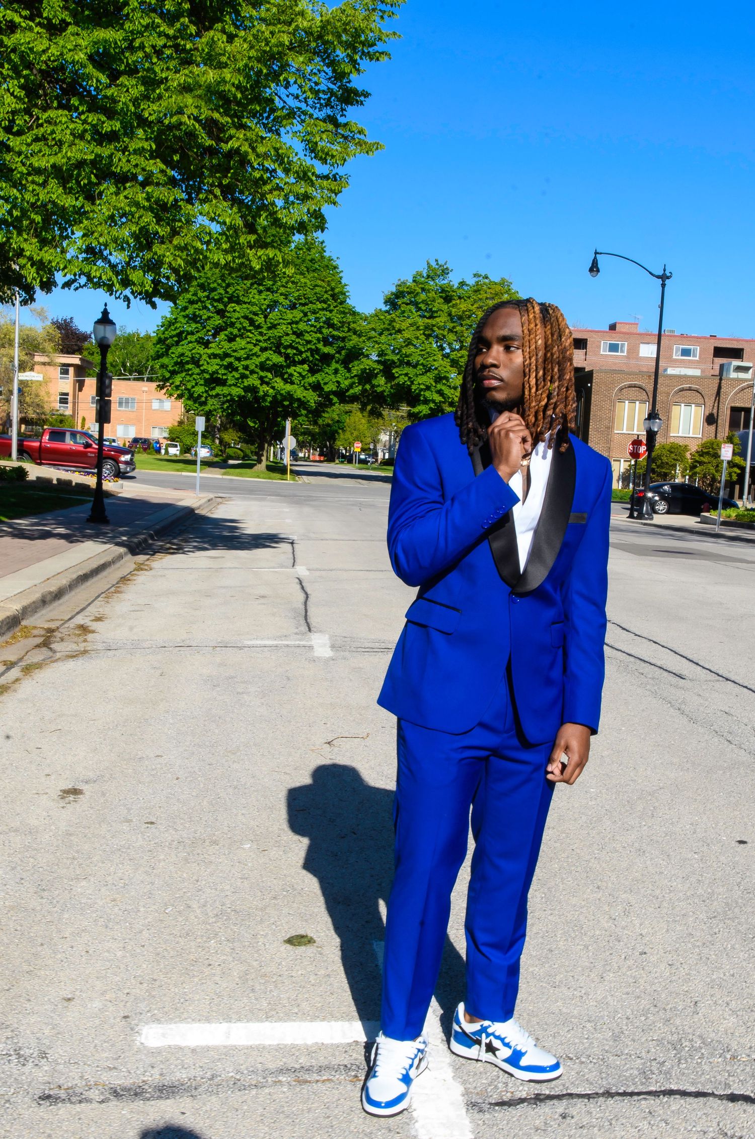 Person in bright blue suit striking poses on urban street with trees in background.