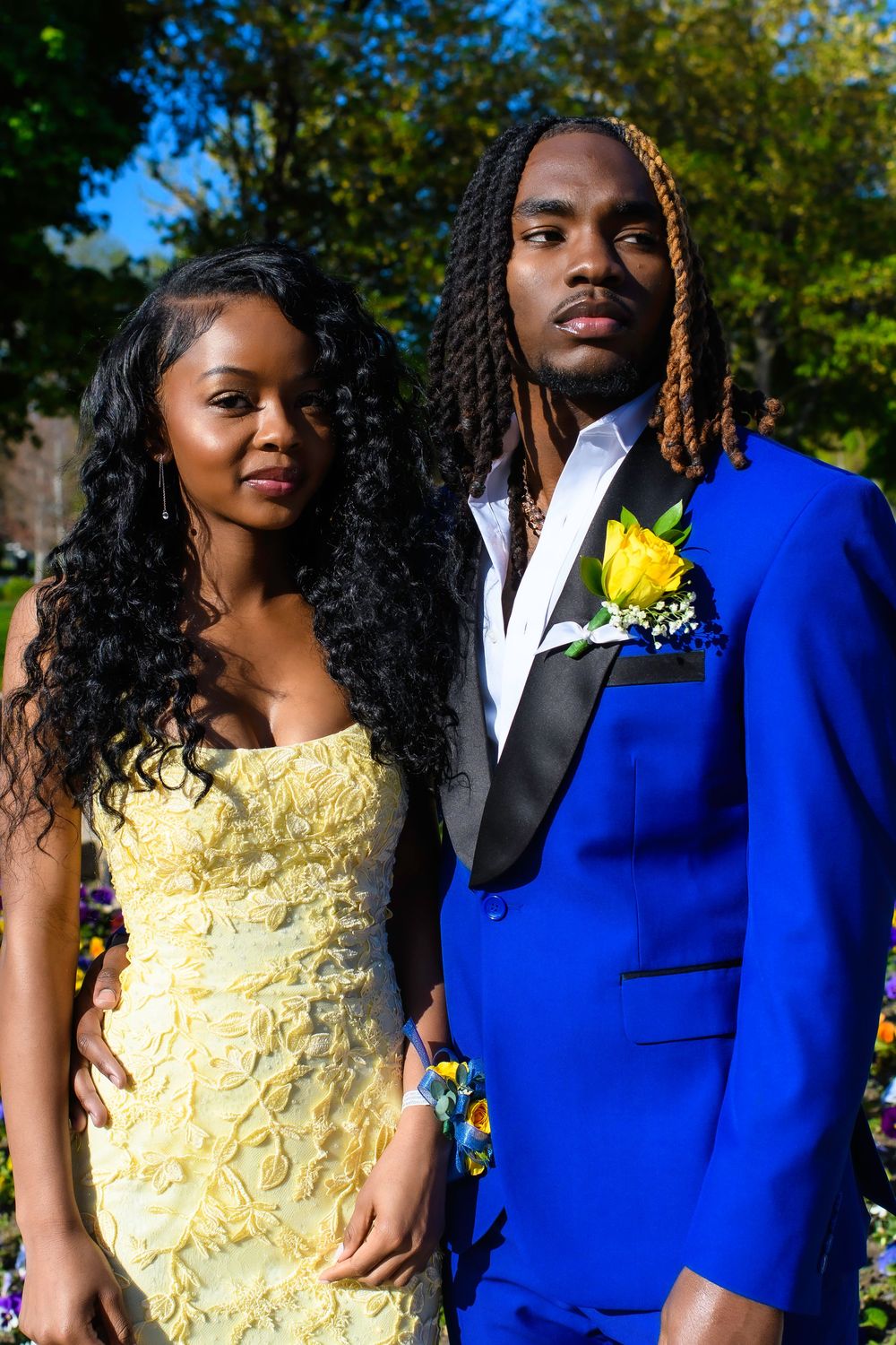 Couple in vibrant yellow dress and royal blue suit pose together outdoors for formal photos.