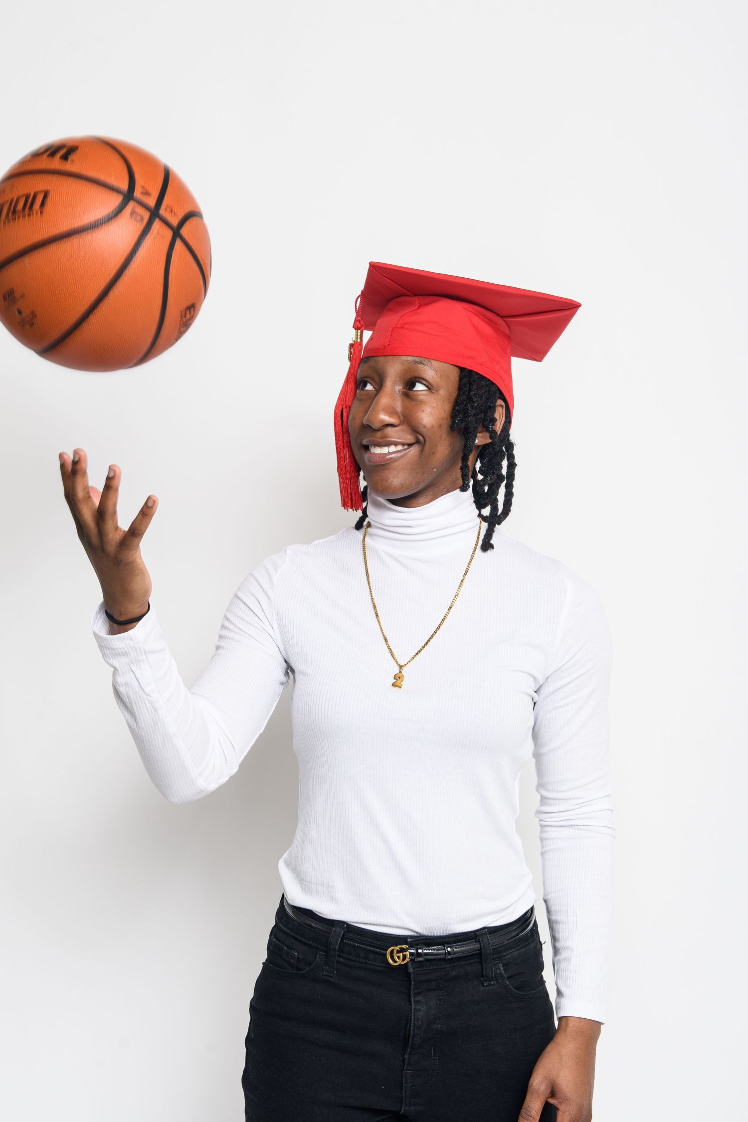 Graduate in red cap playfully posing with basketball in studio against white background.