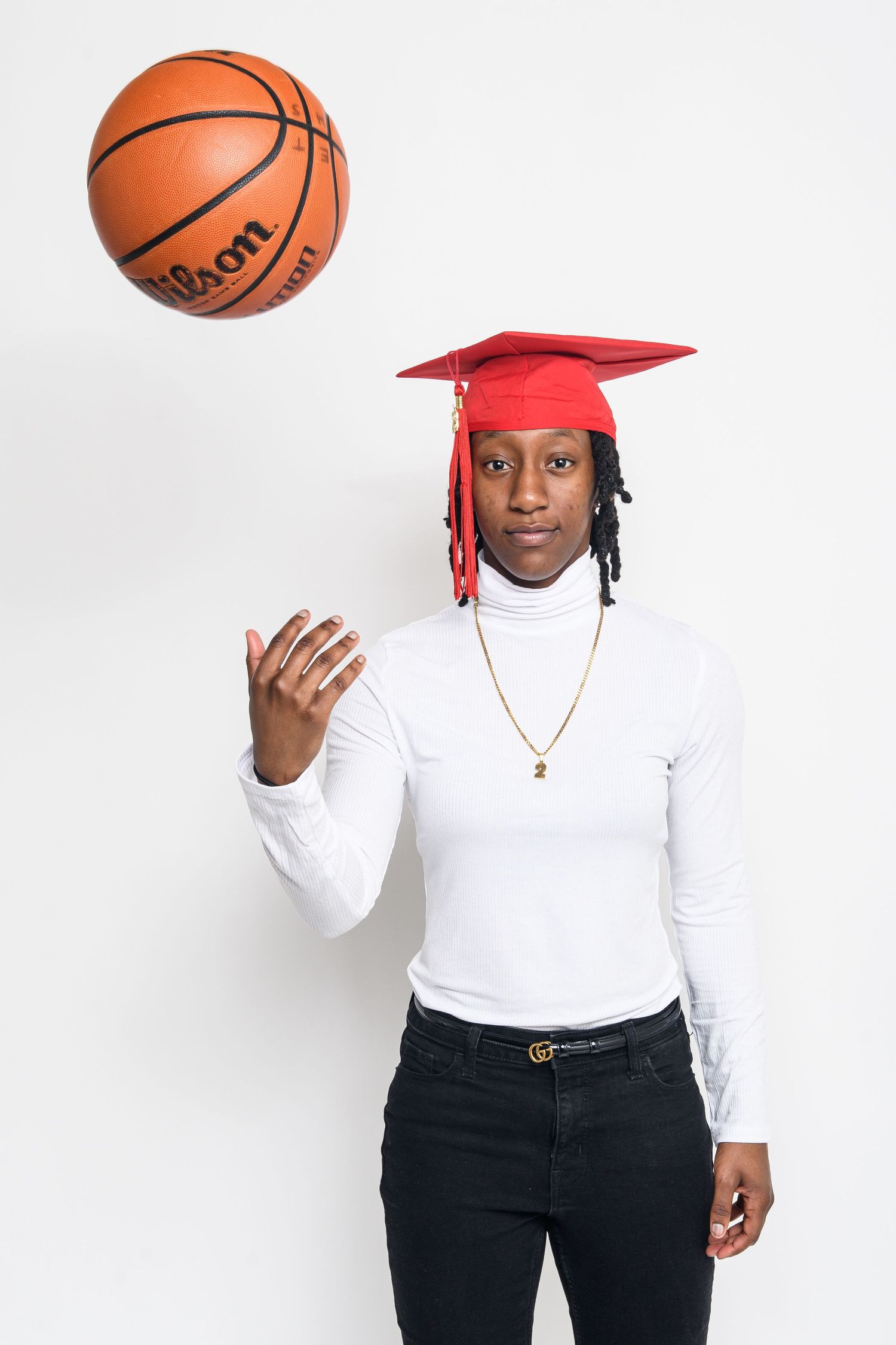 Graduate in red cap and white turtleneck throwing basketball in sequence against white backdrop.
