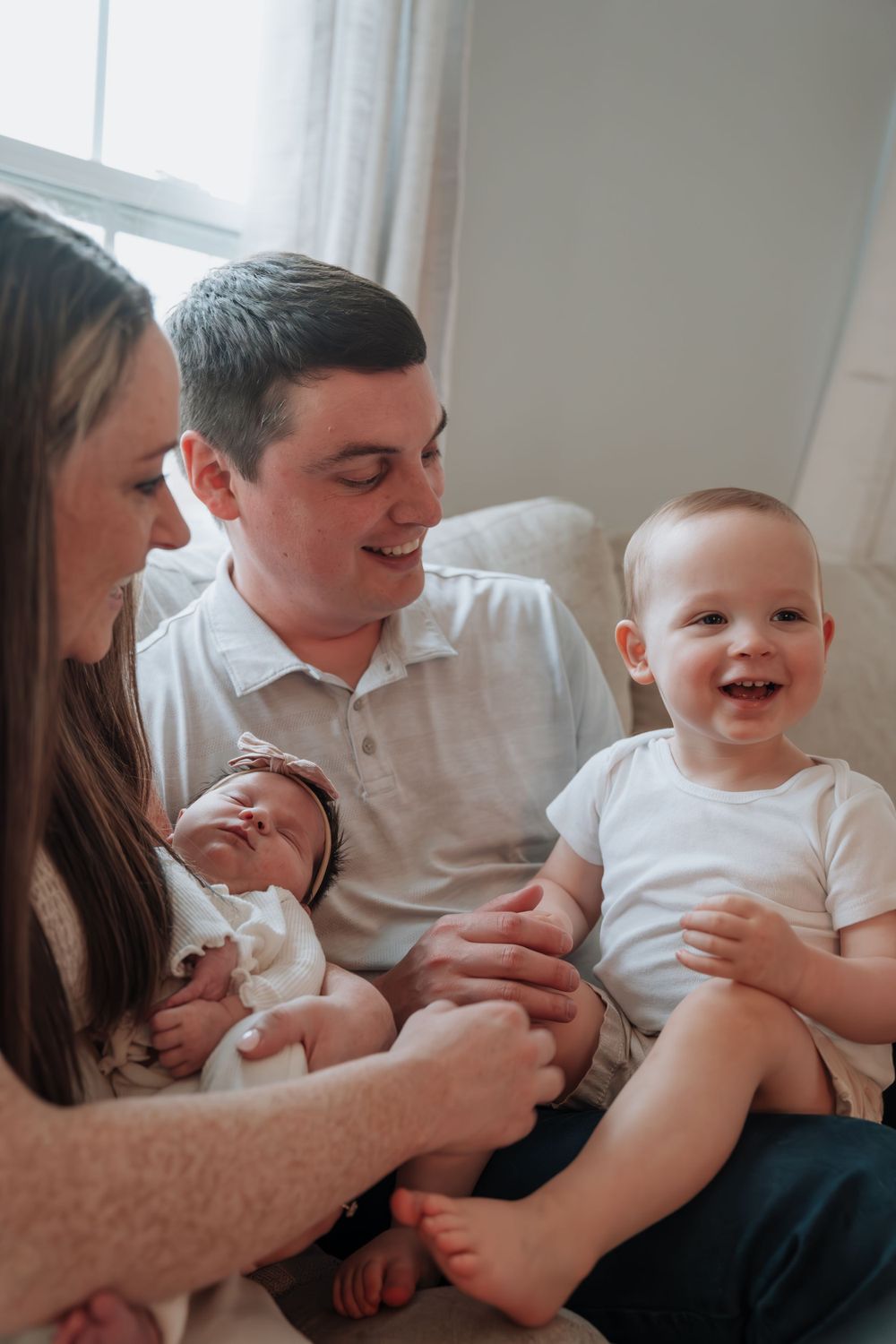 Happy family with newborn baby and toddler son sitting together in a bright cozy room.