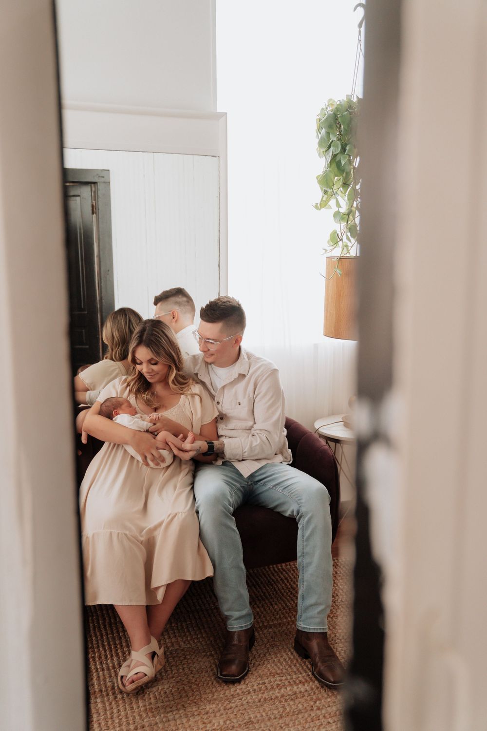 Happy family with newborn baby sitting together on a couch viewed through a doorway in a bright home.