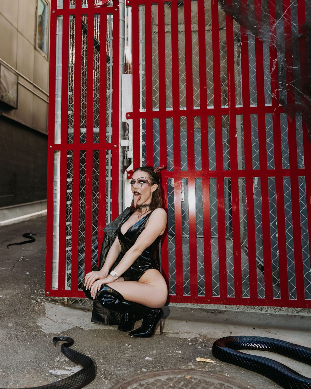 Moody fashion portrait against bright red industrial gates featuring contrast between dark outfit and vibrant background.