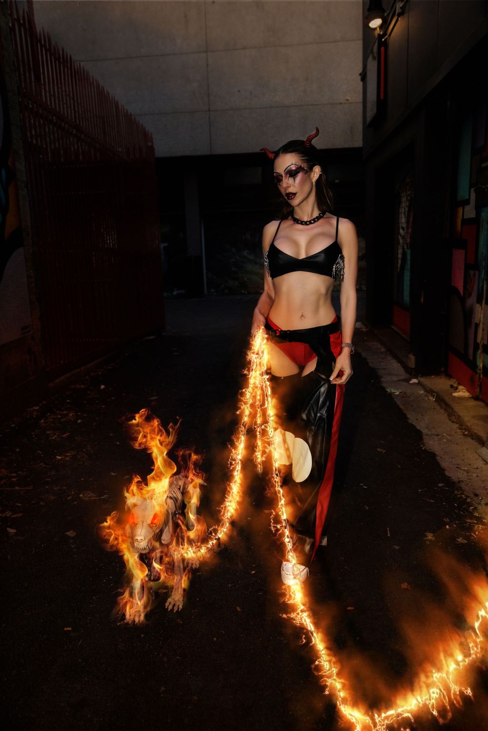 A dramatic fire performance in a dark alley features a person in dark clothing surrounded by flames and fiery trails.