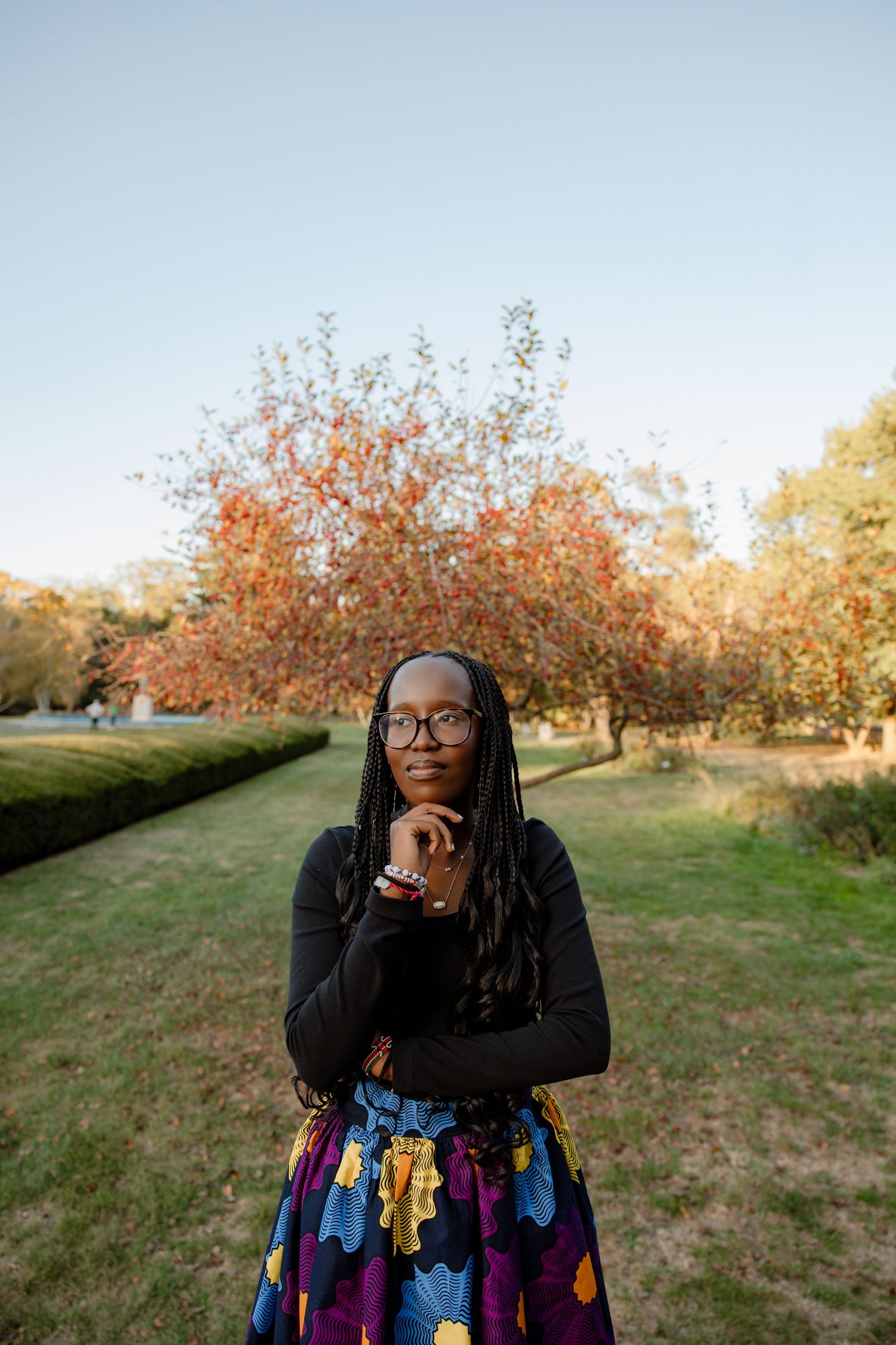 A person in a colorful floral skirt poses thoughtfully in an autumn park setting.