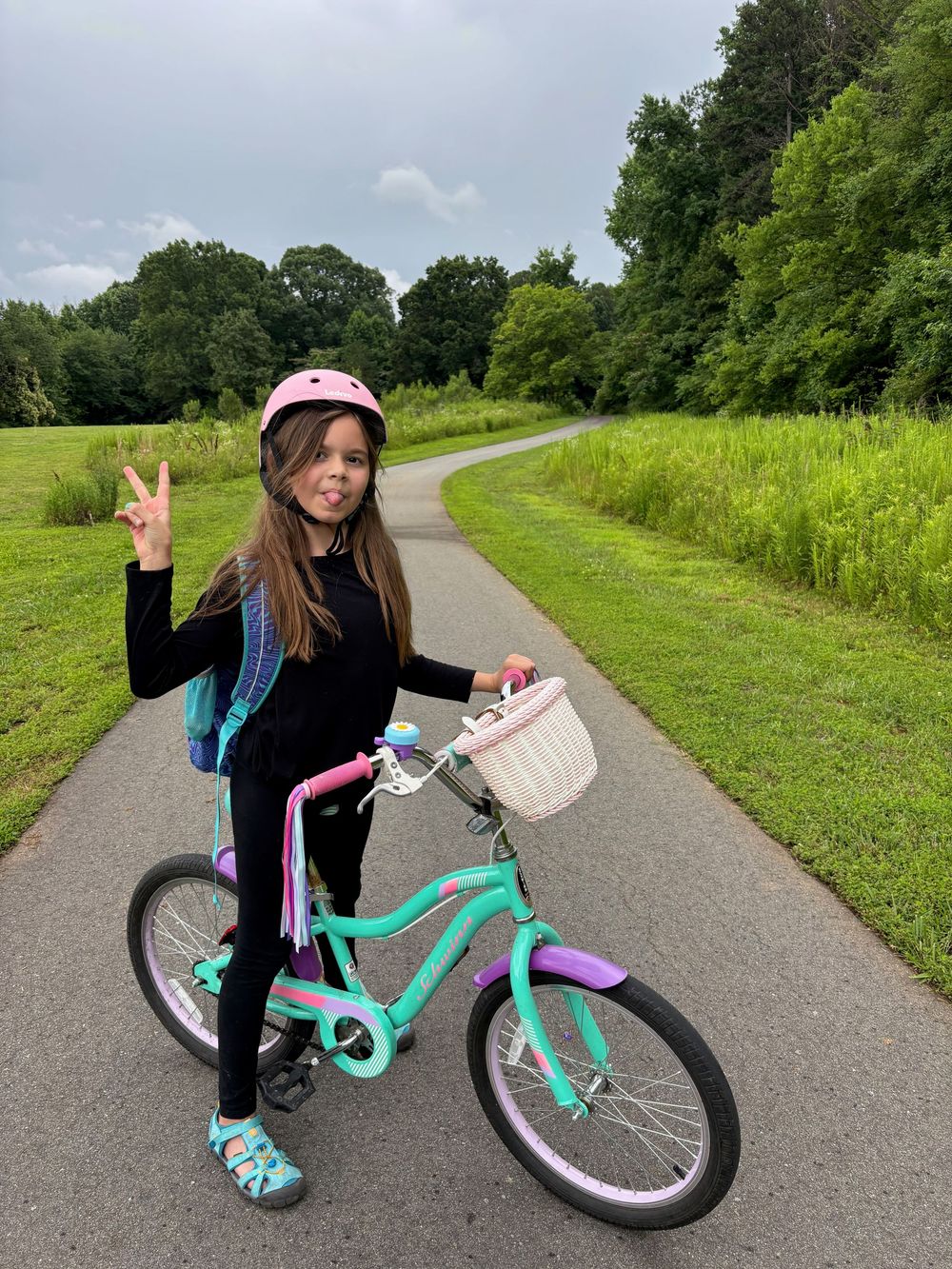 A person riding a mint green bicycle on a paved trail surrounded by lush summer greenery and trees.