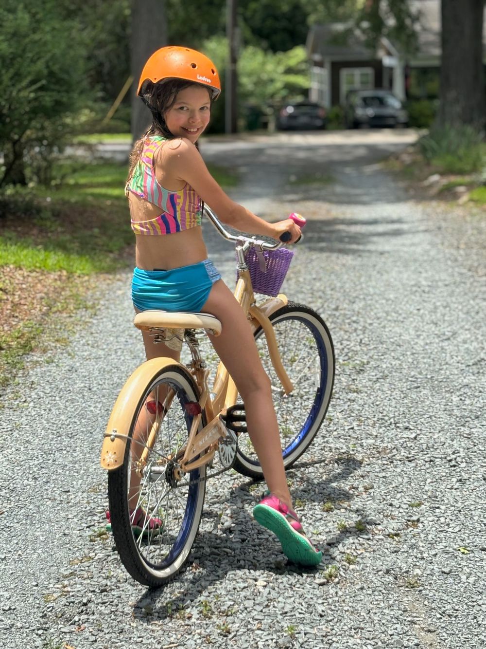 A child rides a blue and yellow balance bike on a gravel path during a sunny summer day.
