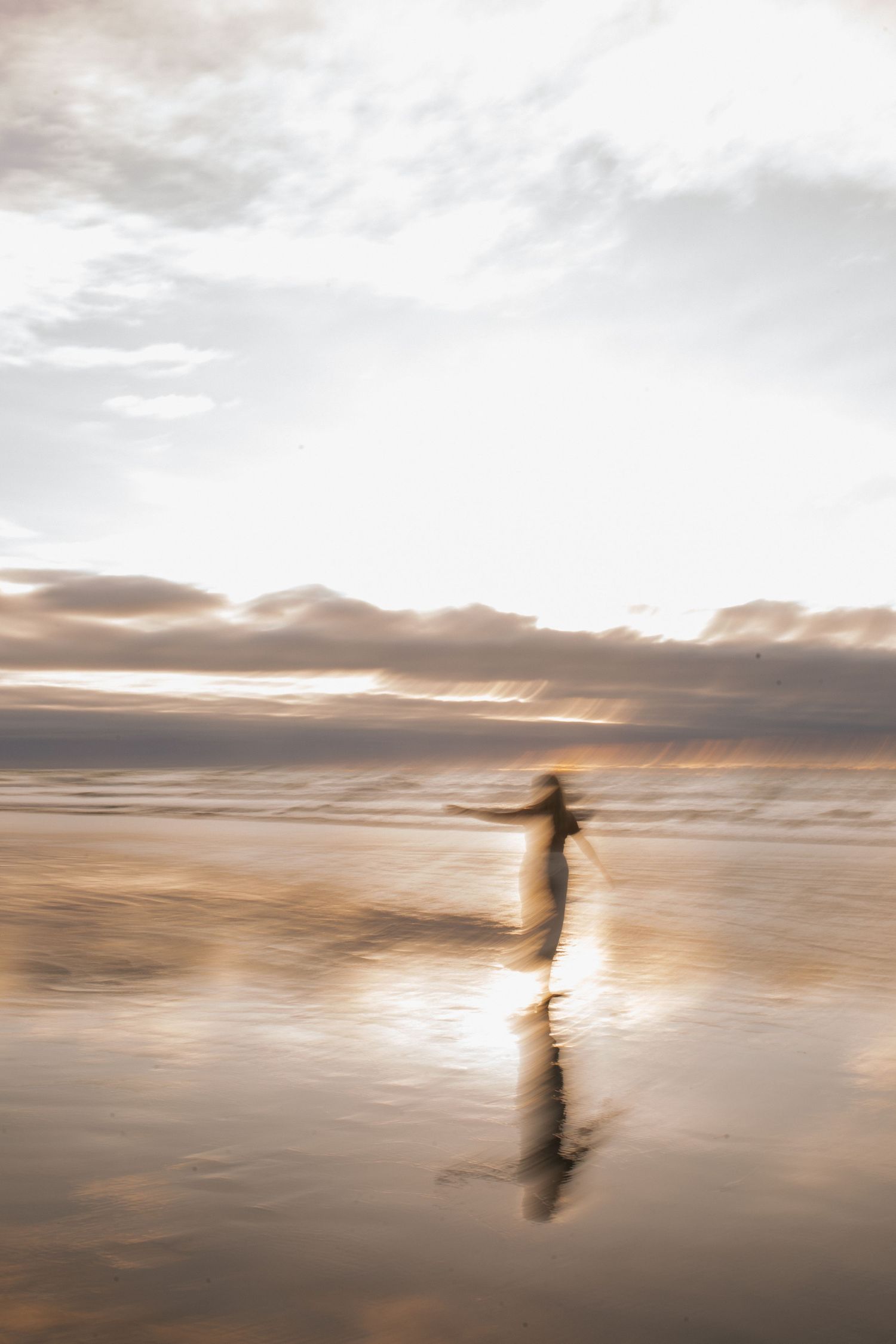 Blurred silhouette of person running on reflective wet beach at dramatic sunset.
