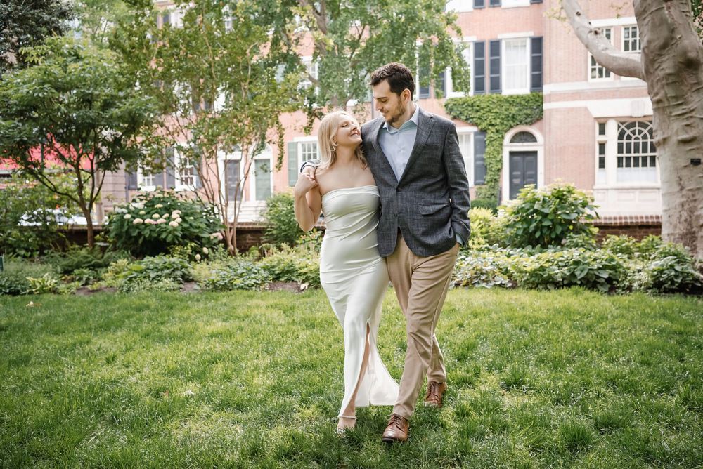 An engaged couple walks through a garden setting on a bright summer day in Philadelphia's Rittenhouse Square during their engagement session