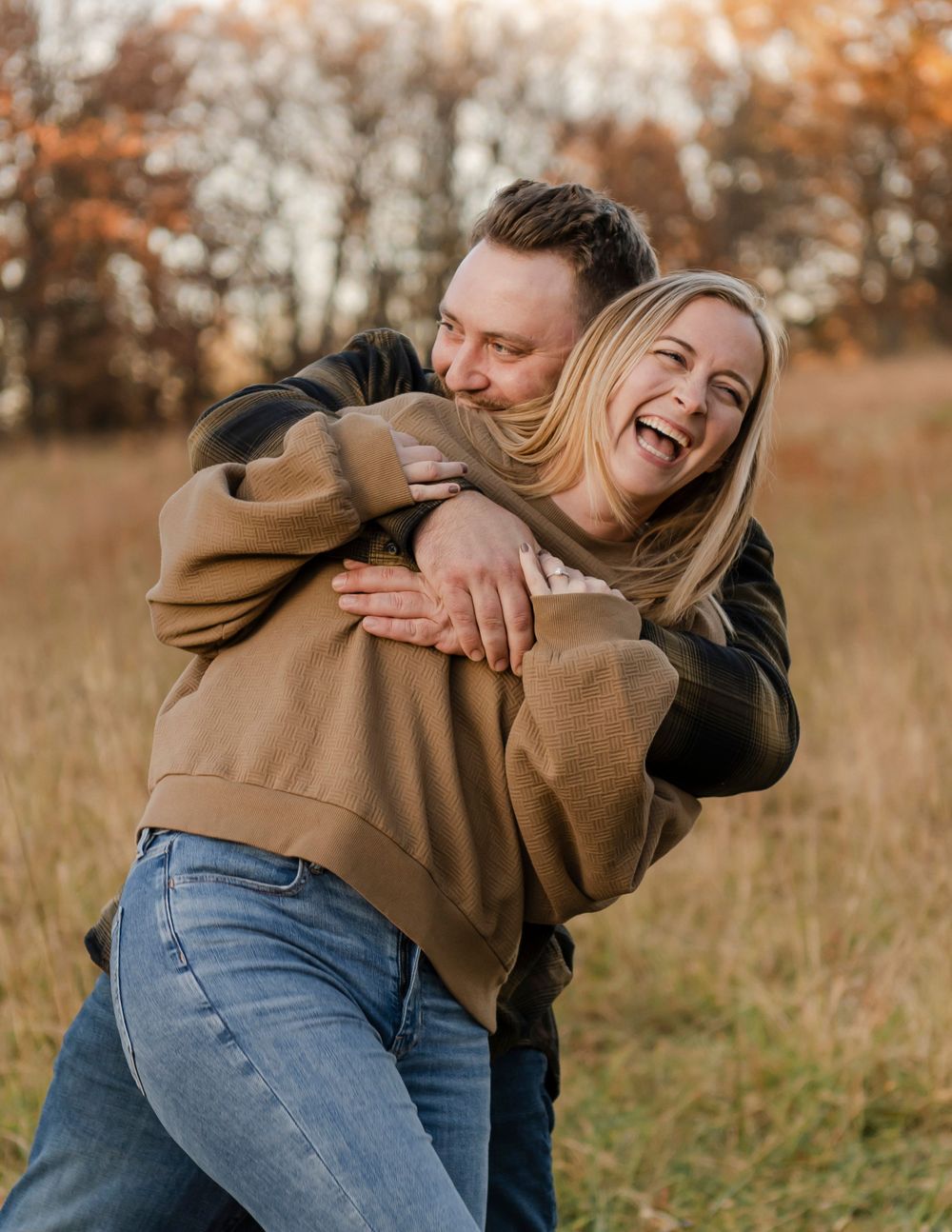 Candid moment of a joyful couple embracing and laughing together in an autumn field with golden grass.