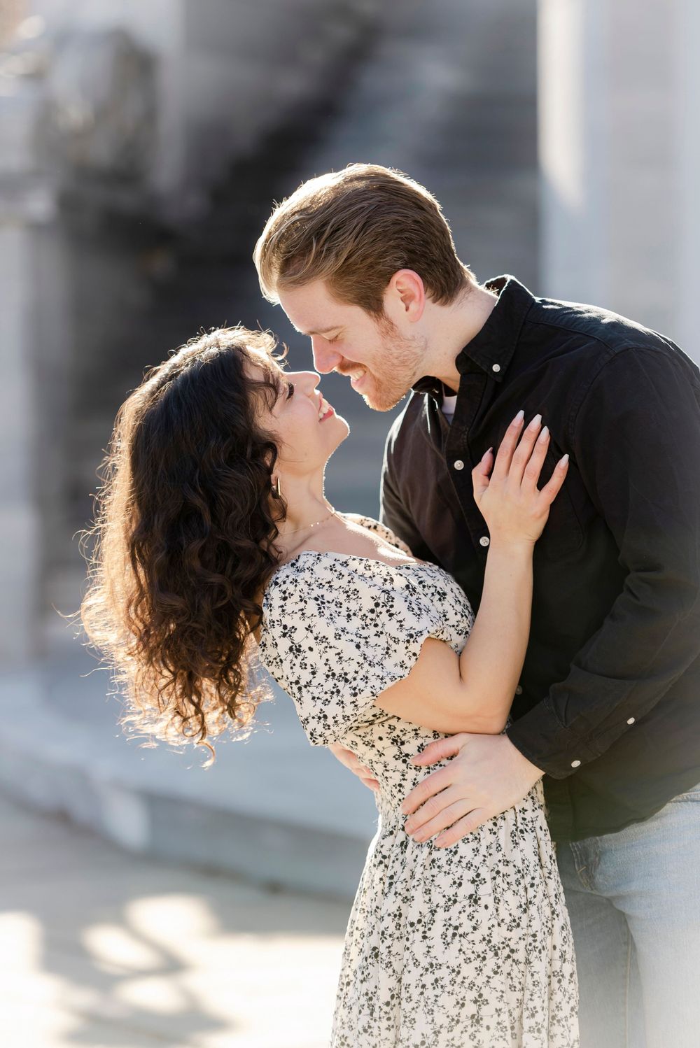 Romantic couple in an intimate embrace outdoors, with her wearing a floral dress and him in a dark button-up shirt.