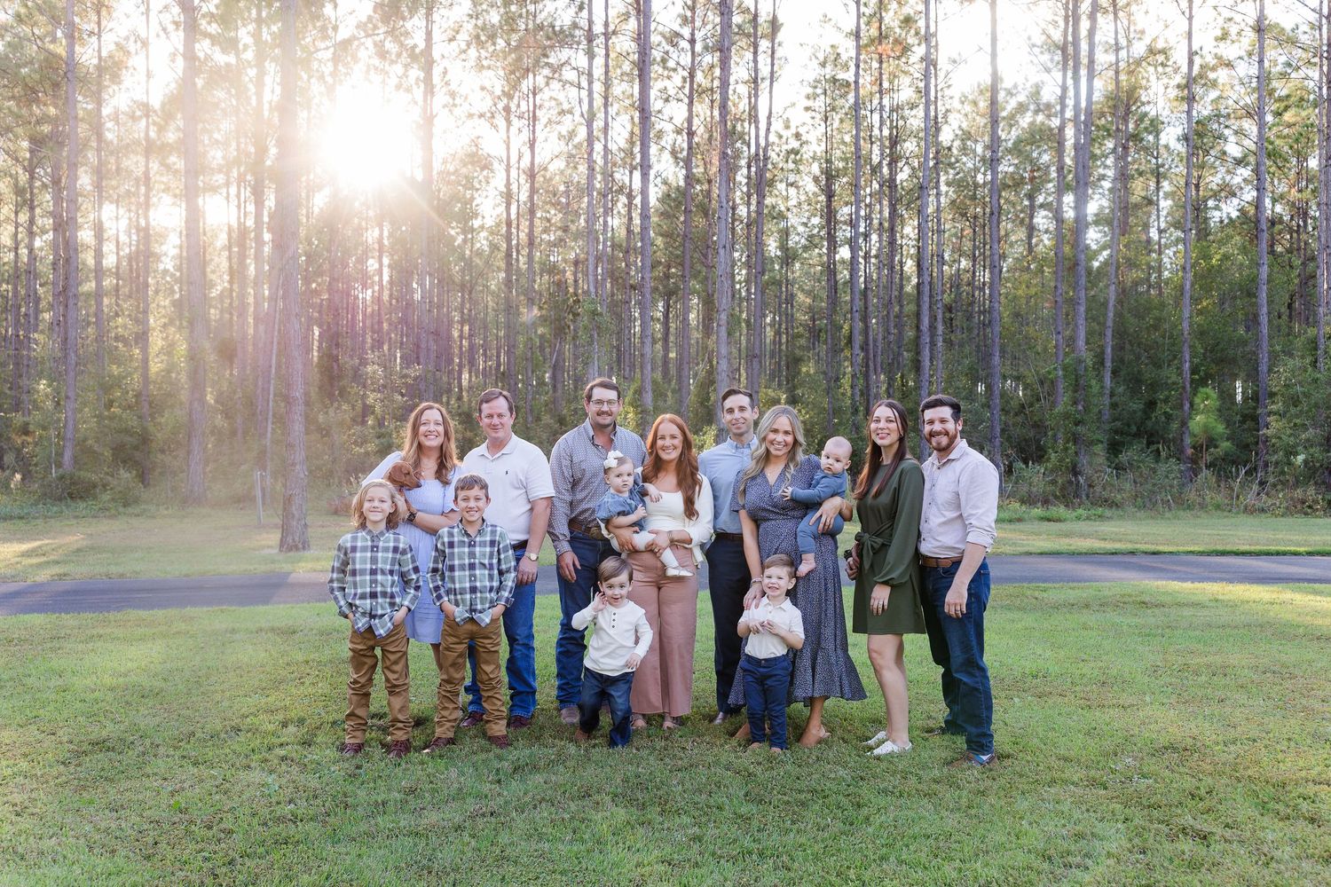 Extended family portrait session in a sunlit pine forest clearing.