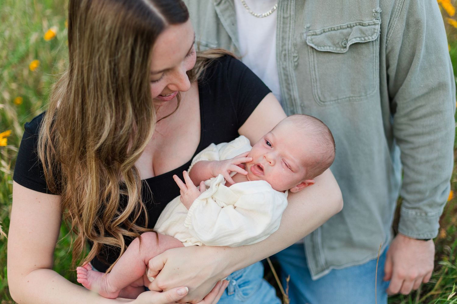 Tender moments between parent and newborn baby outdoors among yellow wildflowers.