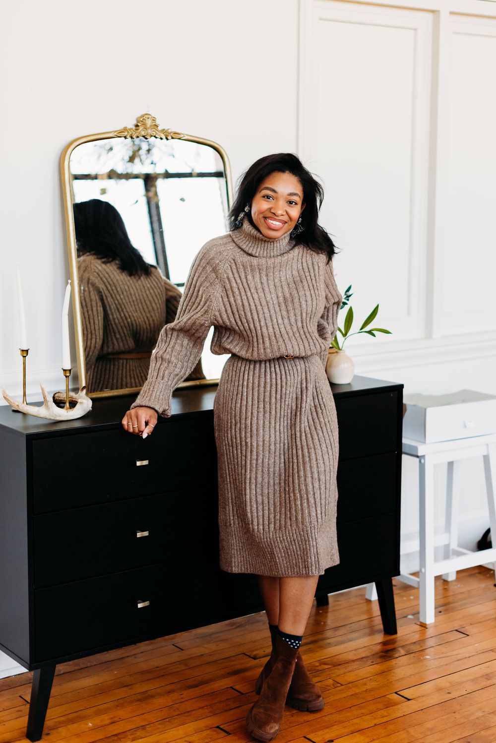 Cozy neutral turtleneck sweater dress with brown boots styled in elegant home interior with vintage mirror and dresser.