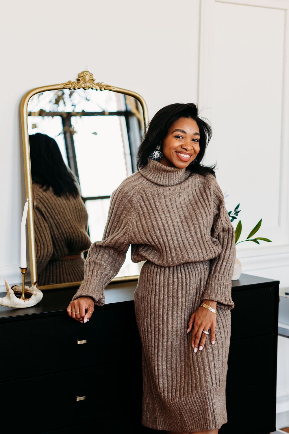 A cozy brown turtleneck sweater dress ensemble shown next to an elegant gold-framed mirror in a bright interior space.
