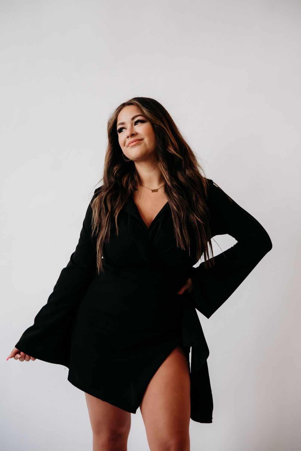 Long-sleeved black mini dress with flared sleeves and v-neck design against white background.