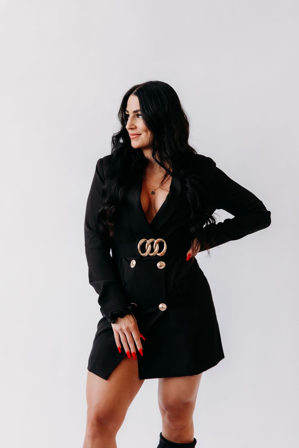 Stylish black blazer dress with gold belt buckle detail and long sleeves in a modern studio setting.