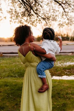 A tender moment captured at sunset shows a figure in a yellow dress holding a small child against a backdrop of trees.