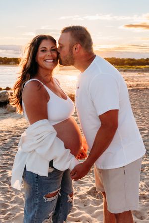 A romantic couple shares a tender moment on the beach at sunset while wearing casual white and denim attire.