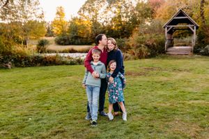 A loving family enjoys an autumn afternoon together on a grassy lawn with a wooden gazebo in the background.