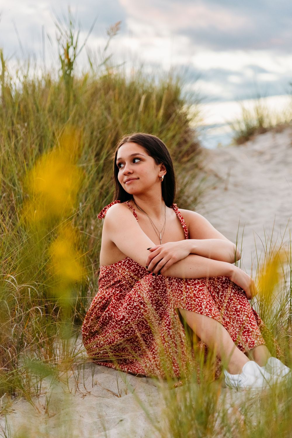 A summer portrait in a floral sundress sitting among beach grass and dunes on a cloudy day.