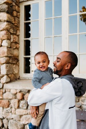 A tender moment between parent and child smiling together outside a stone building with large white windows.