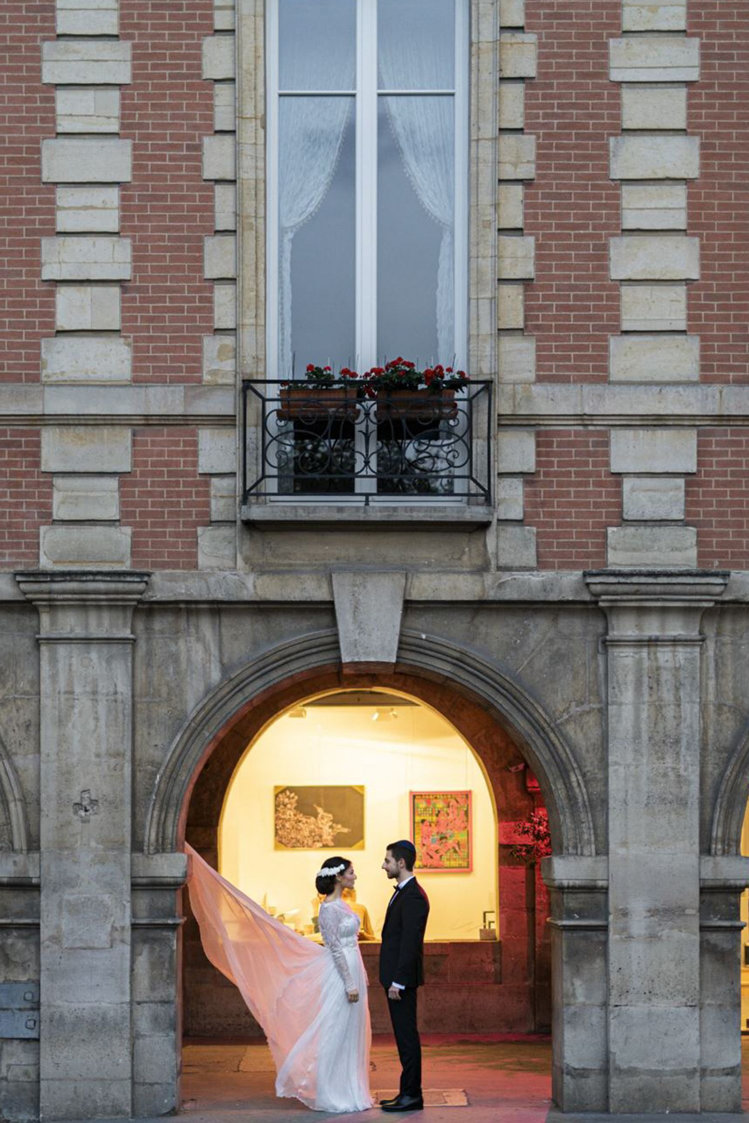 Couple de mariés sous une arche de la place des Vosges à Paris, scène romantique et architecturale.