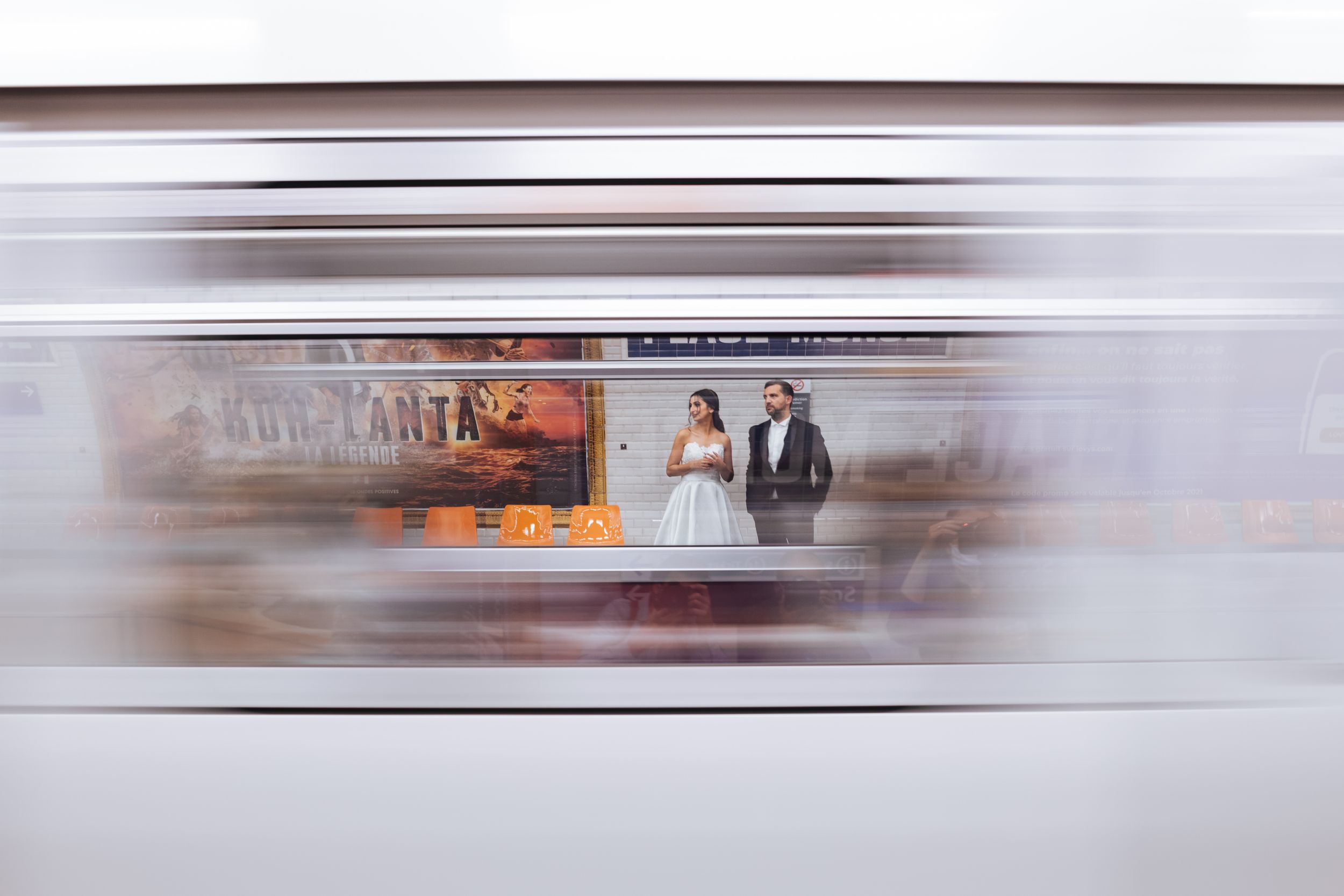 Couple de mariés photographié derrière un métro parisien en mouvement, scène urbaine dynamique et moderne.