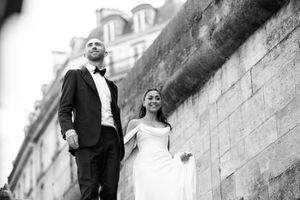 Mariés posant contre un mur en pierre en noir et blanc, portrait élégant et intemporel.