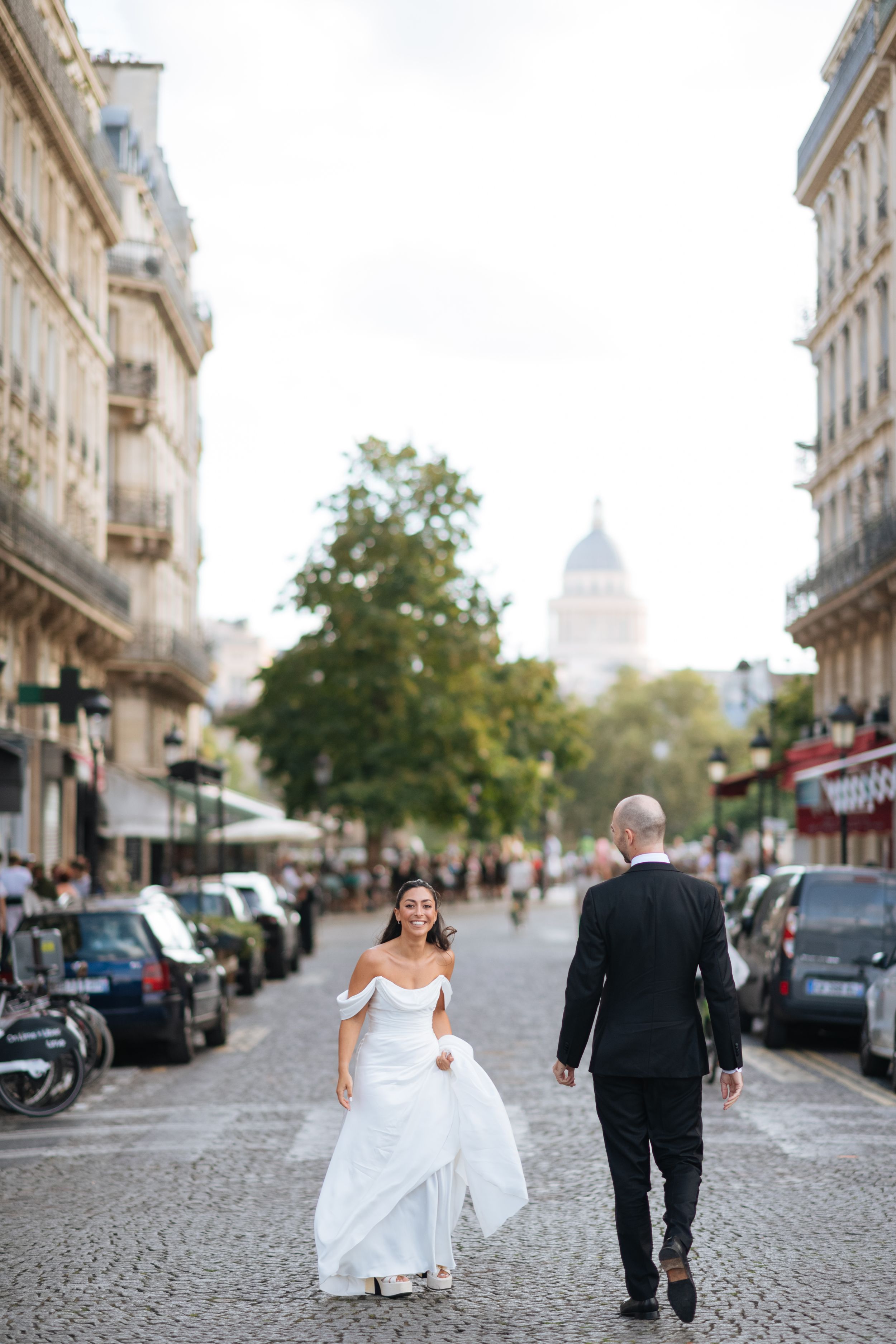 Couple de mariés marchant main dans la main dans une rue pavée de Paris, ambiance urbaine romantique.