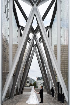 Mariés sous une grande structure métallique graphique, perspective urbaine forte et moderne valorisant la Bibliotheque Francois Mitterand