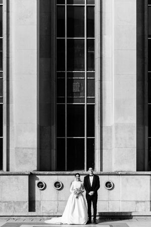 Couple de mariés devant une façade moderne en verre et métal, contraste élégant entre architecture et romance, place du Trocadero à Paris