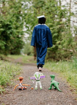 A sequence of colorful toy dinosaurs lined up on a dirt path with someone walking away in the distance.
