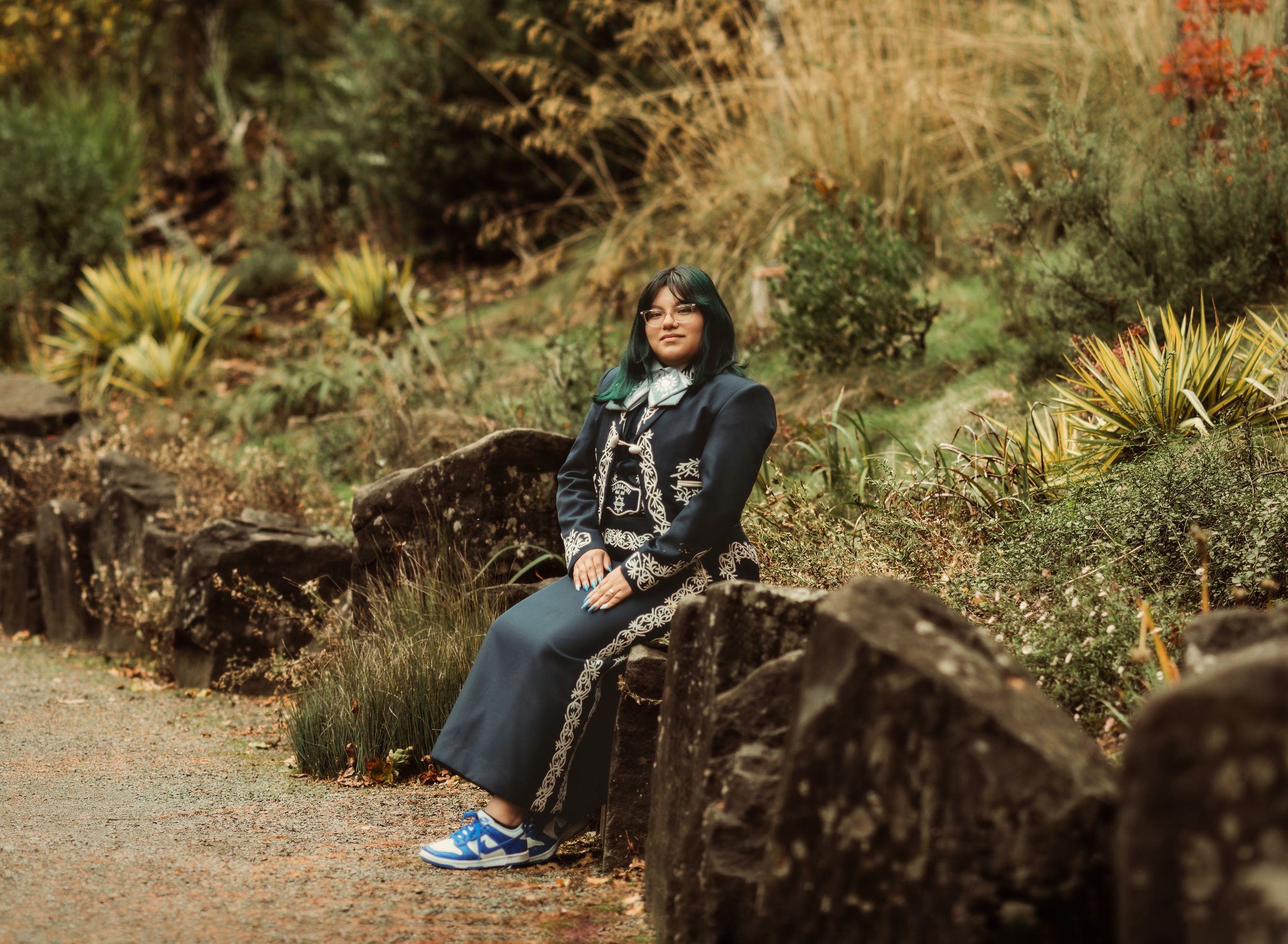 A person sits on a wooden bench in a garden surrounded by lush greenery and natural landscaping.