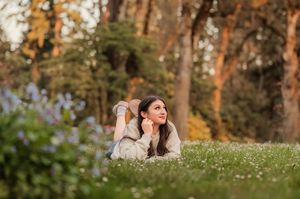 A couple relaxes on a blanket in a sunny autumn park with fallen leaves and tall trees around them.