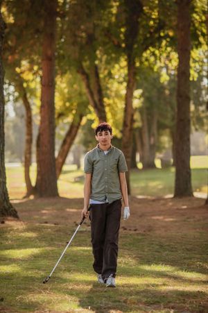 A golfer stands on a wooded course during golden hour, holding a club while surrounded by tall trees in warm sunlight.