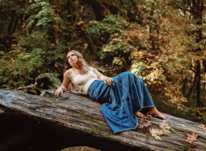 Woman in blue wide-leg pants reclining on a mossy log in an autumn forest setting.