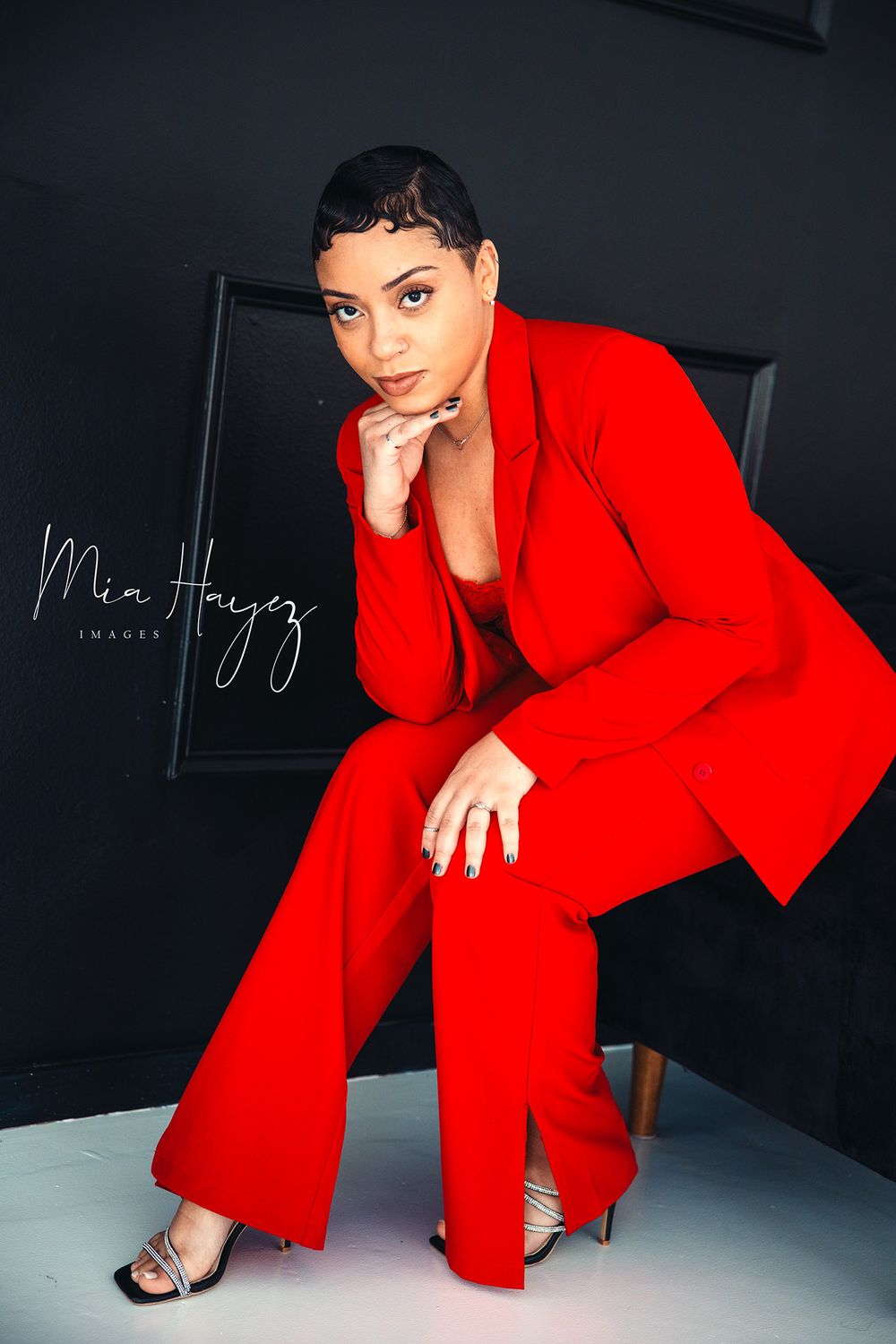 Professional fashion photoshoot featuring a vibrant red power suit against a dark studio backdrop.