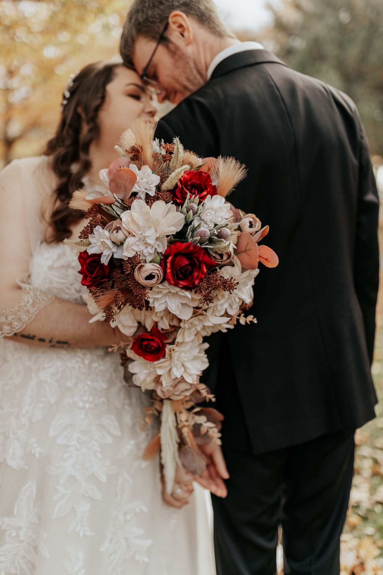 Couple sharing tender moment with vibrant red and white wedding bouquet.