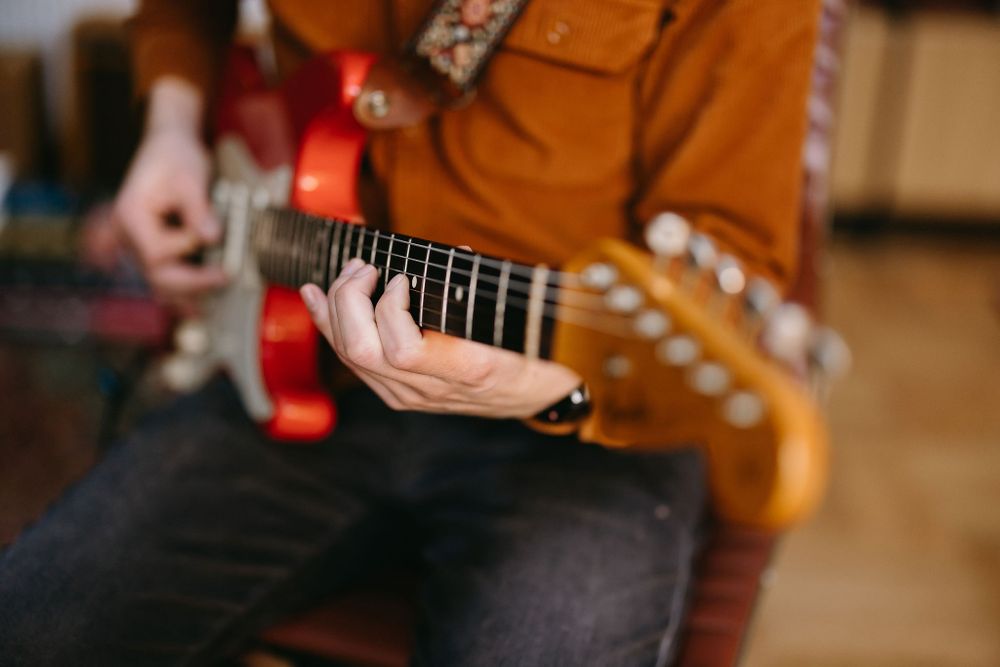 Close-up of hands playing red electric guitar showing detailed finger positioning on fretboard.