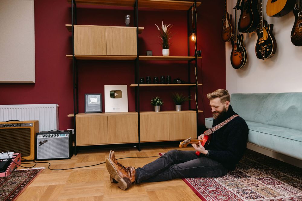 Musician relaxing with guitar in modern music studio with vintage decor and wall-mounted instruments.