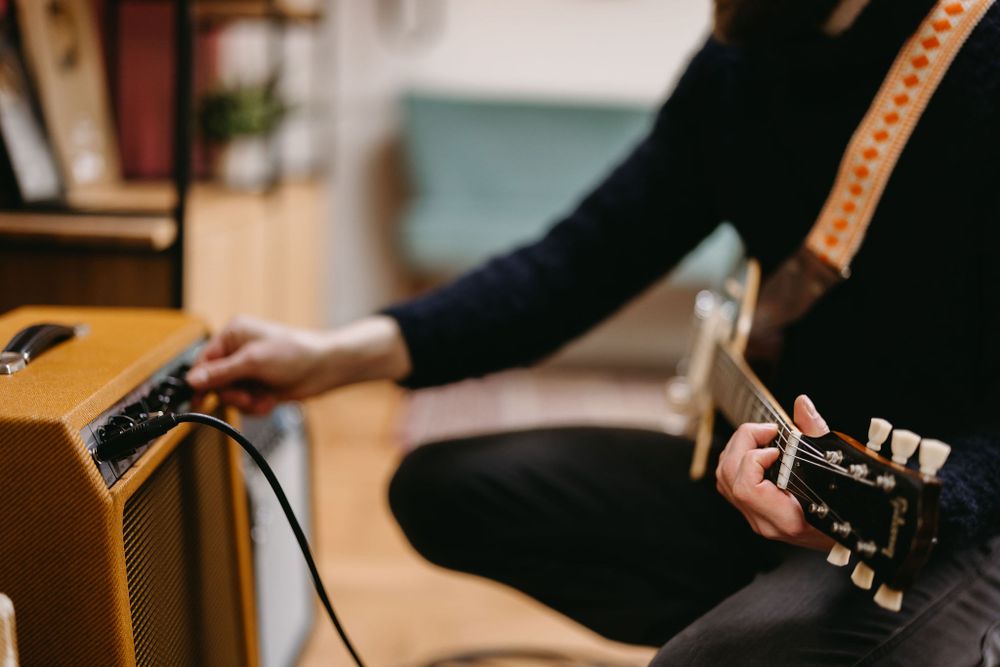 Close-up shot of hands adjusting guitar settings on an amplifier while holding instrument neck.